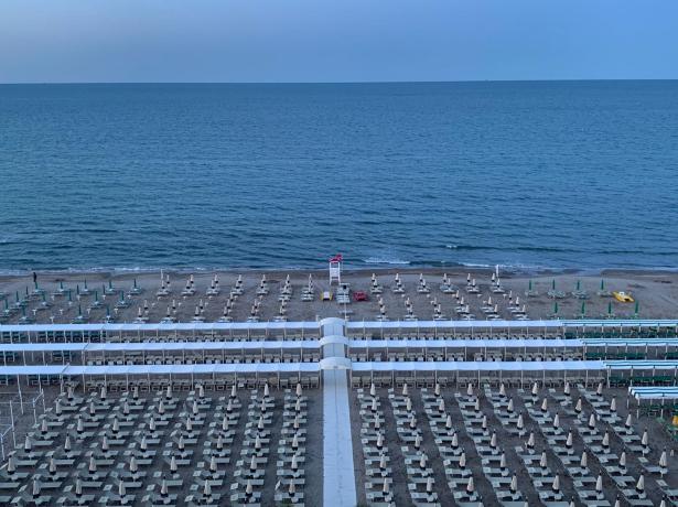 Spiaggia organizzata con ombrelloni e sdraio di fronte al mare calmo.
