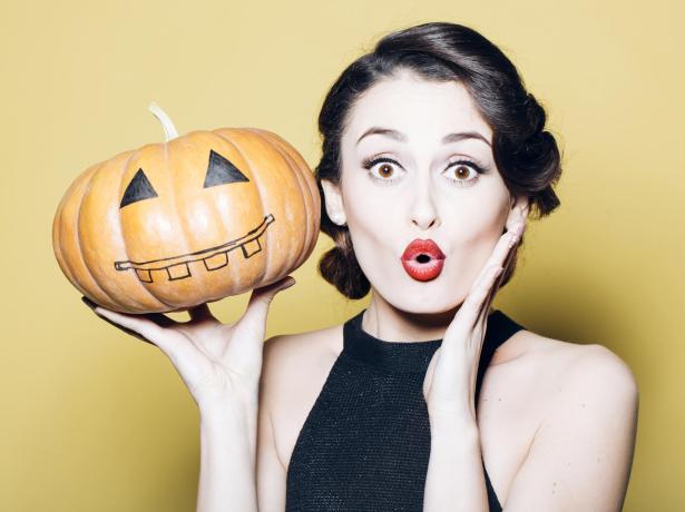 Donna sorpresa con zucca di Halloween decorata.